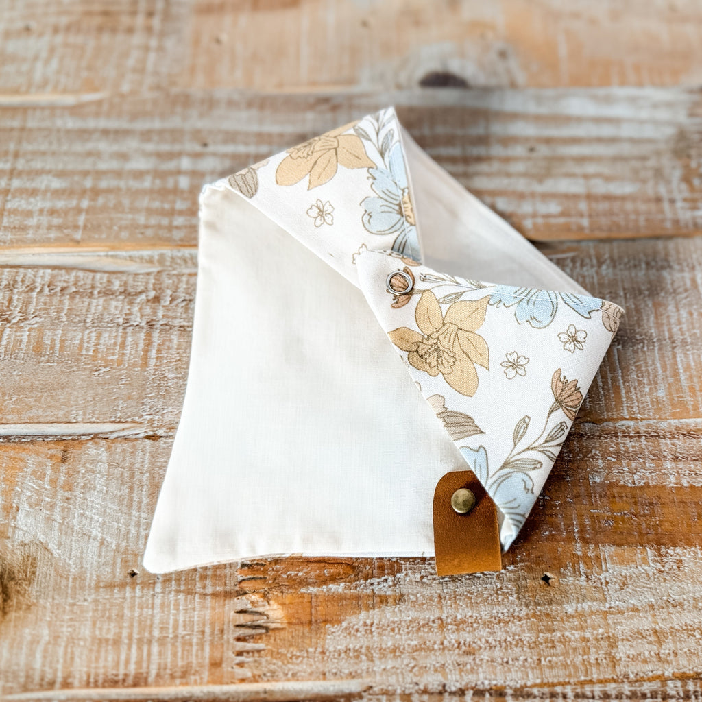 Floral-patterned fabric triangle with a brown leather strap on a wooden surface