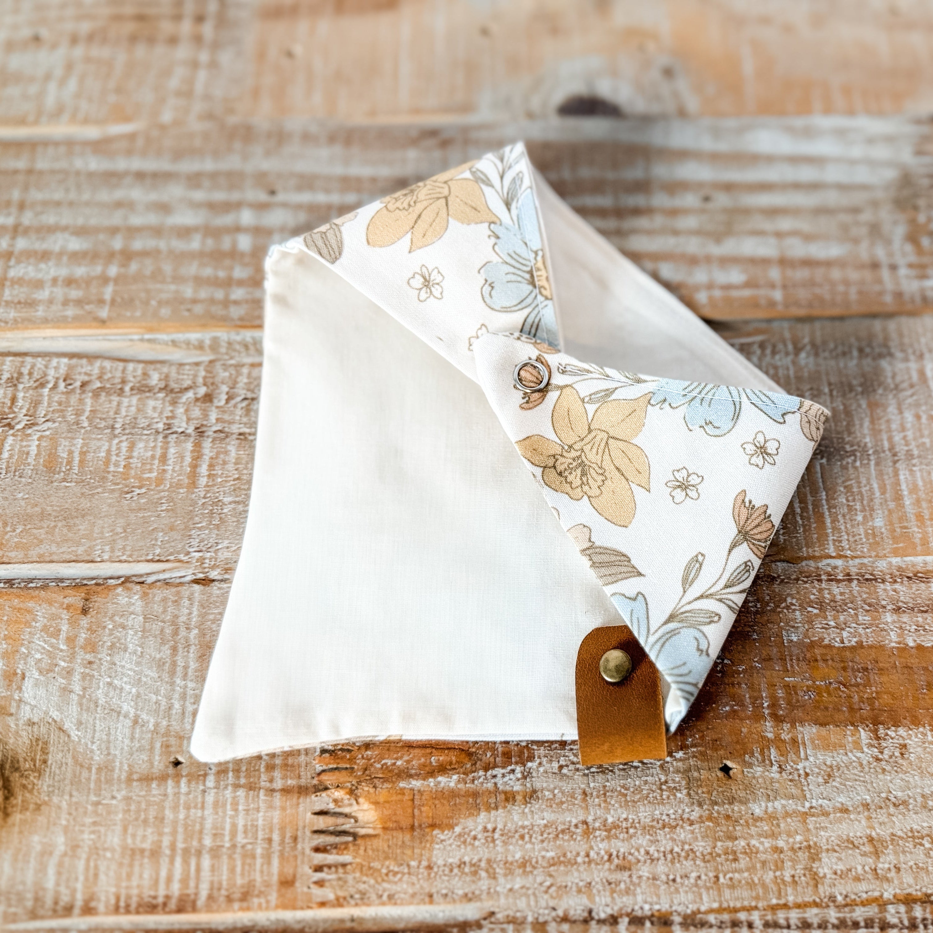 Floral-patterned fabric triangle with a brown leather strap on a wooden surface