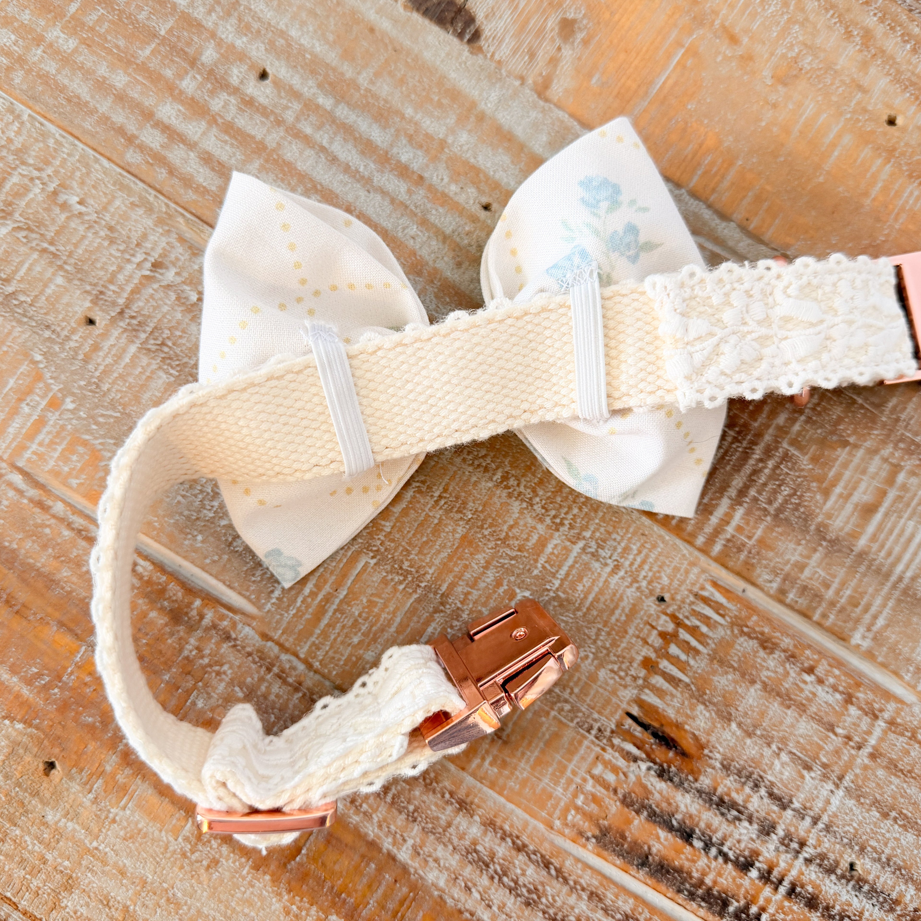 Dog collar with decorative bow and rose gold hardware on a wooden surface