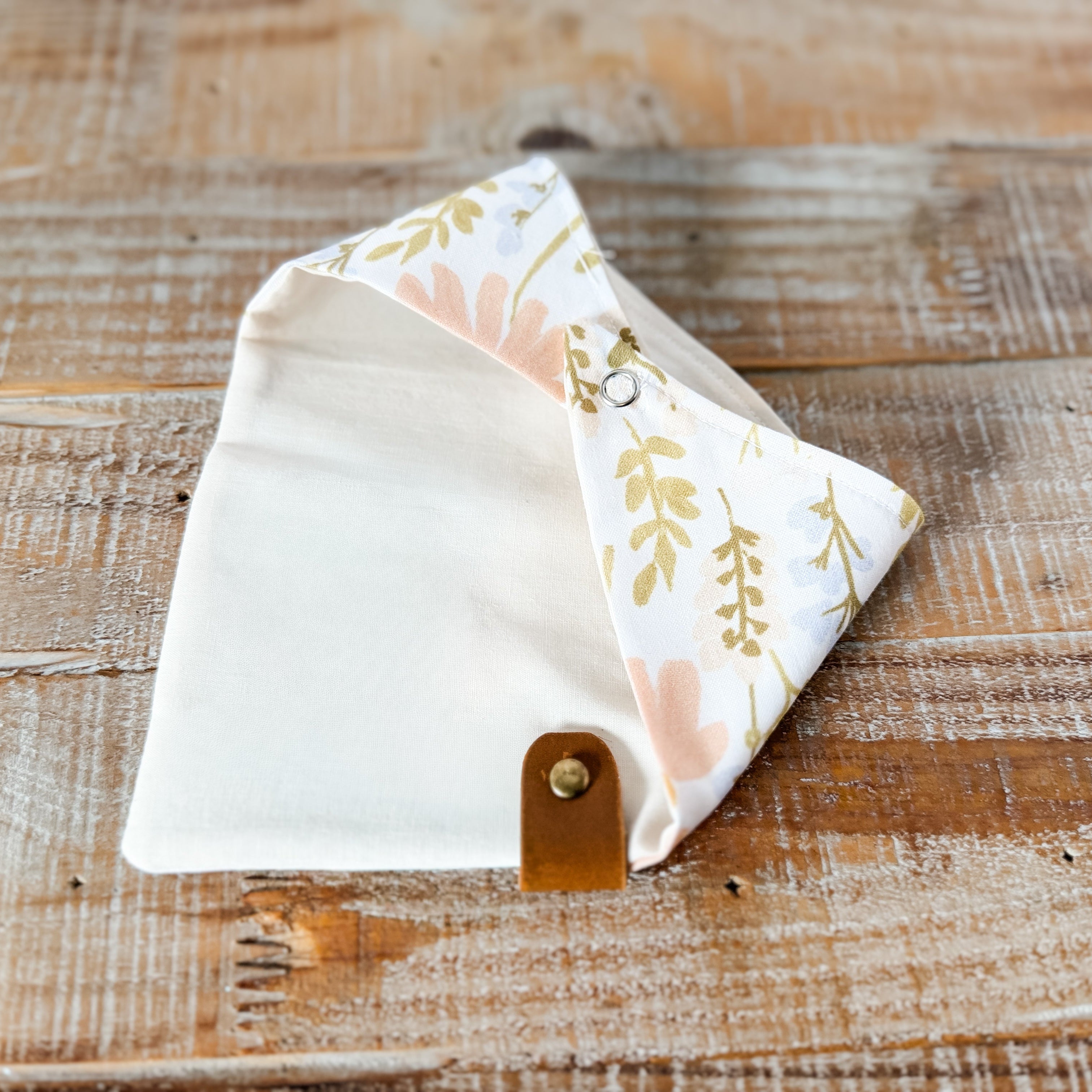 Floral-patterned pouch with a brown leather strap on a wooden surface