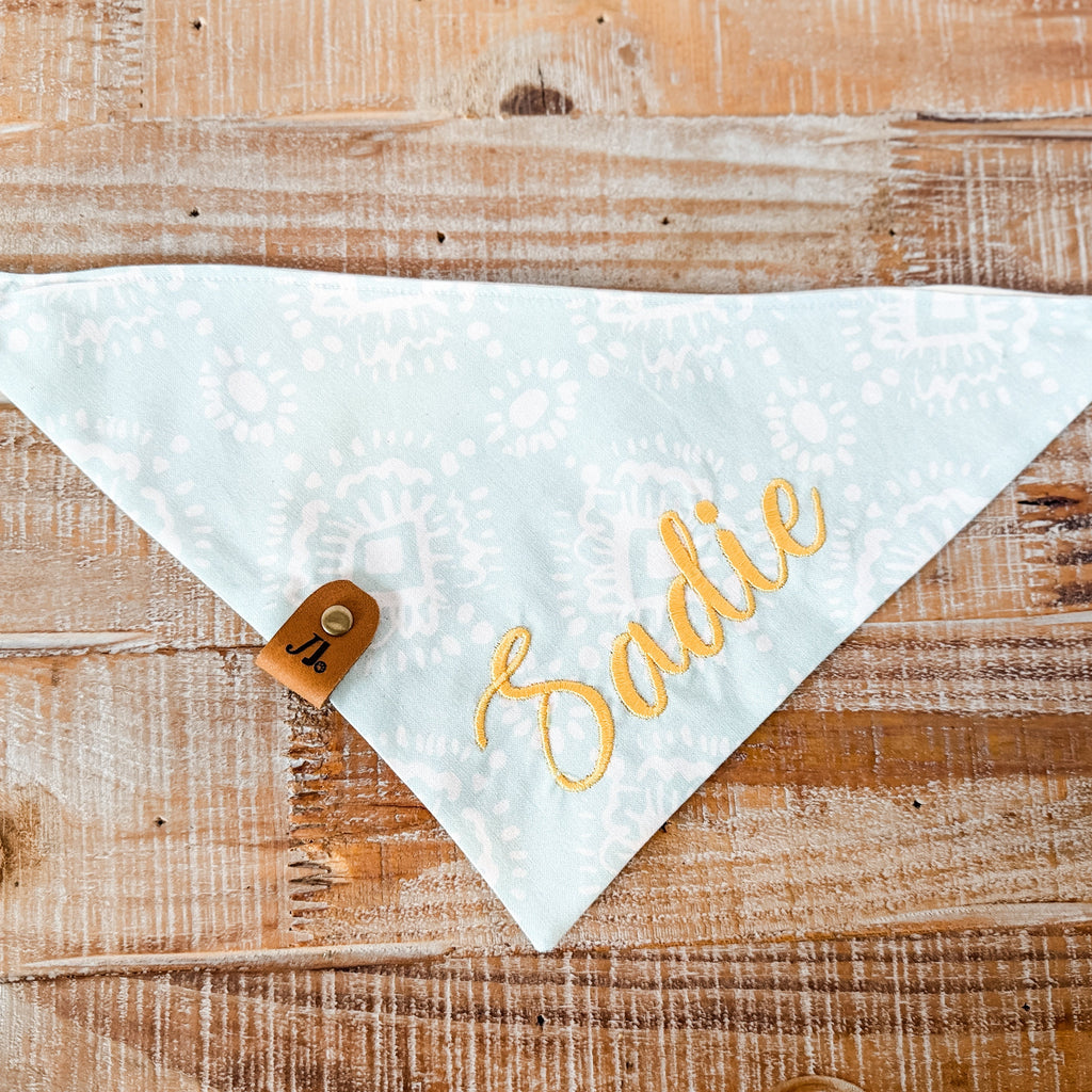 White bandana with 'Sadie' printed in gold on a wooden surface