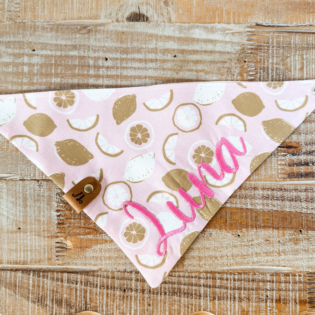 Pink bandana with gold leaf pattern and 'Luna' text on a wooden surface