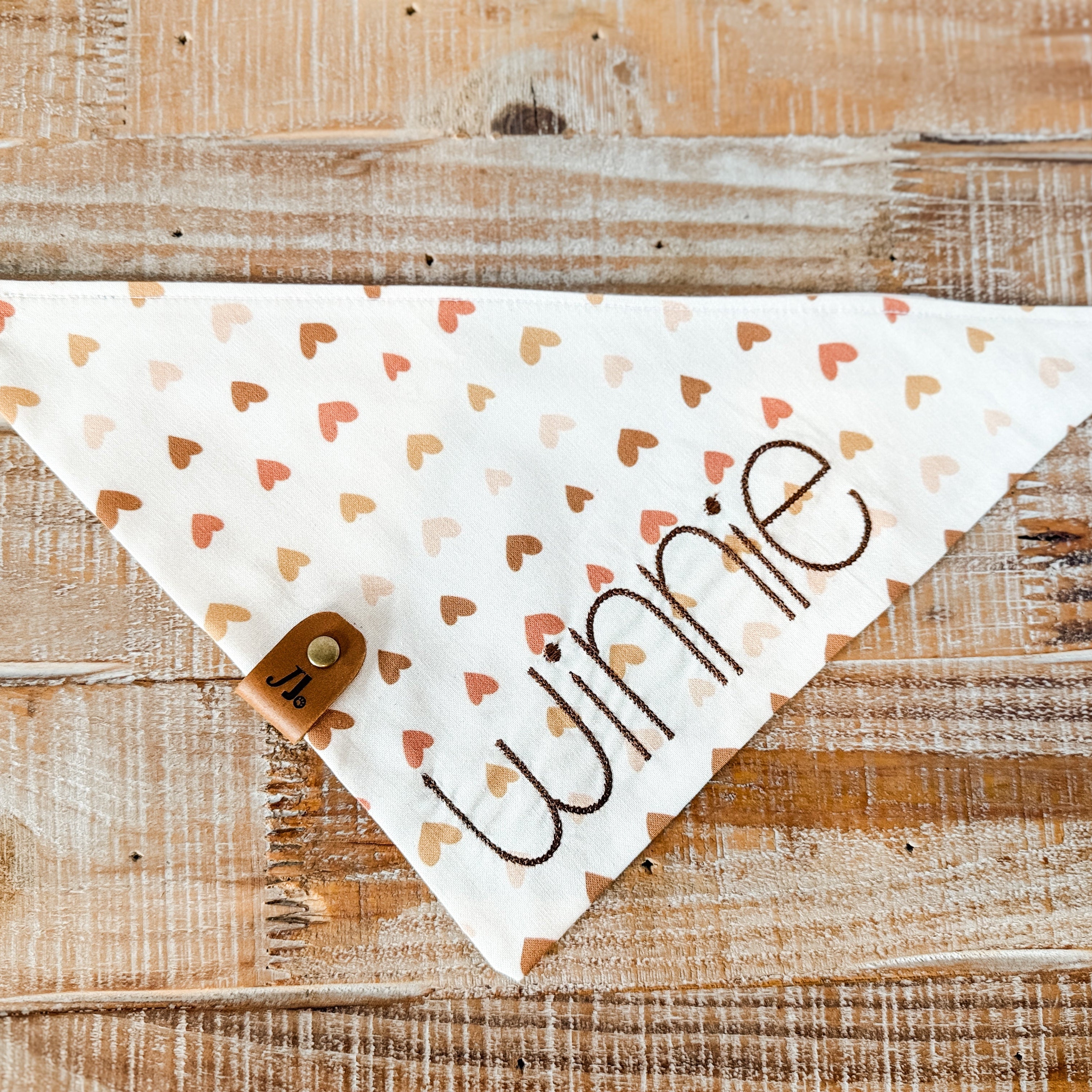 Dog bandana with heart pattern and 'Winnie' text on a wooden surface