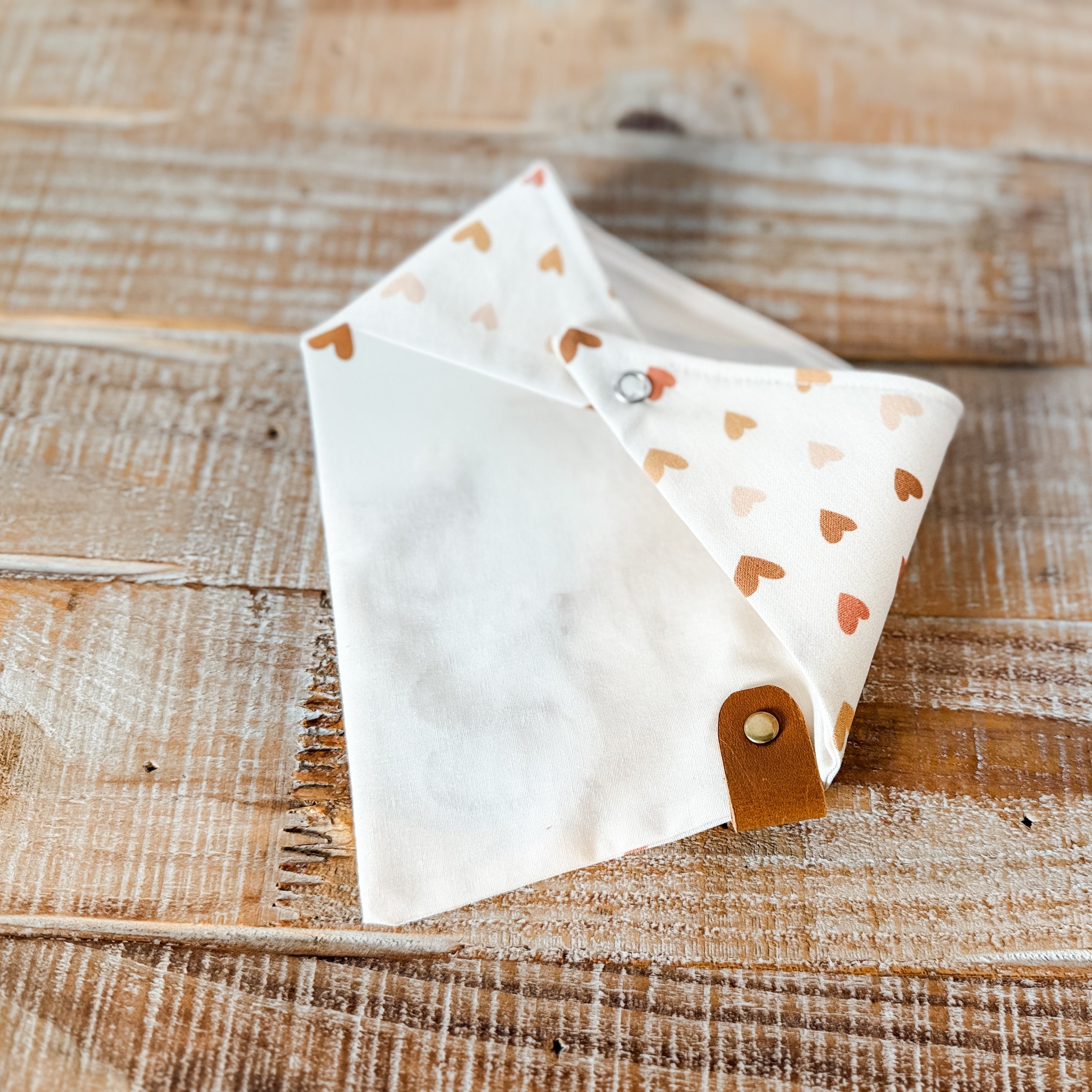 White fabric triangle with brown heart pattern on a wooden surface