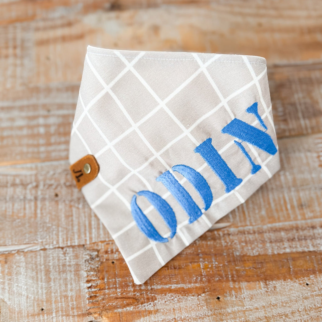 White diamond-shaped scarf with blue embroidered name on a wooden surface