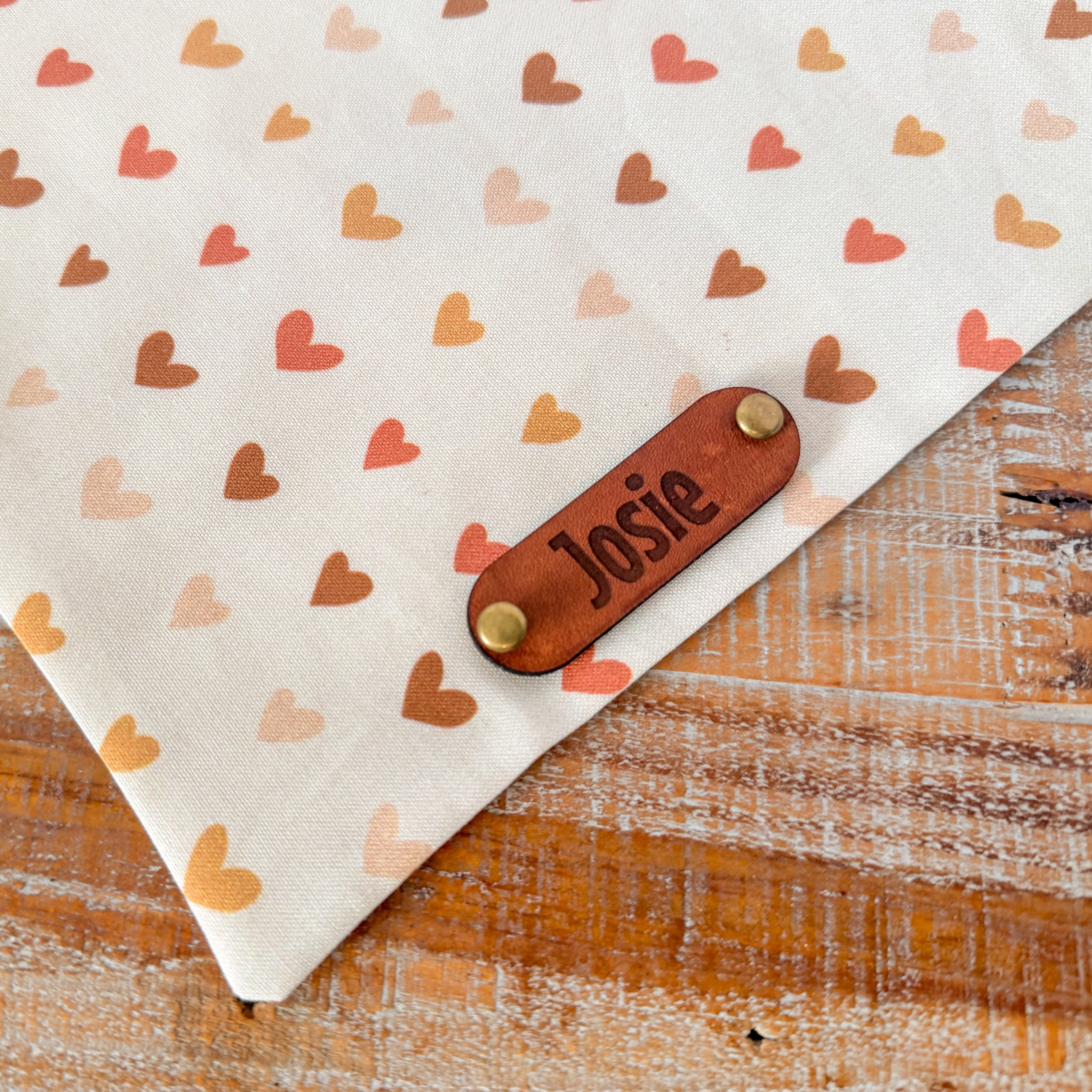 Fabric with heart patterns and a leather patch labeled 'Josie' on a wooden surface