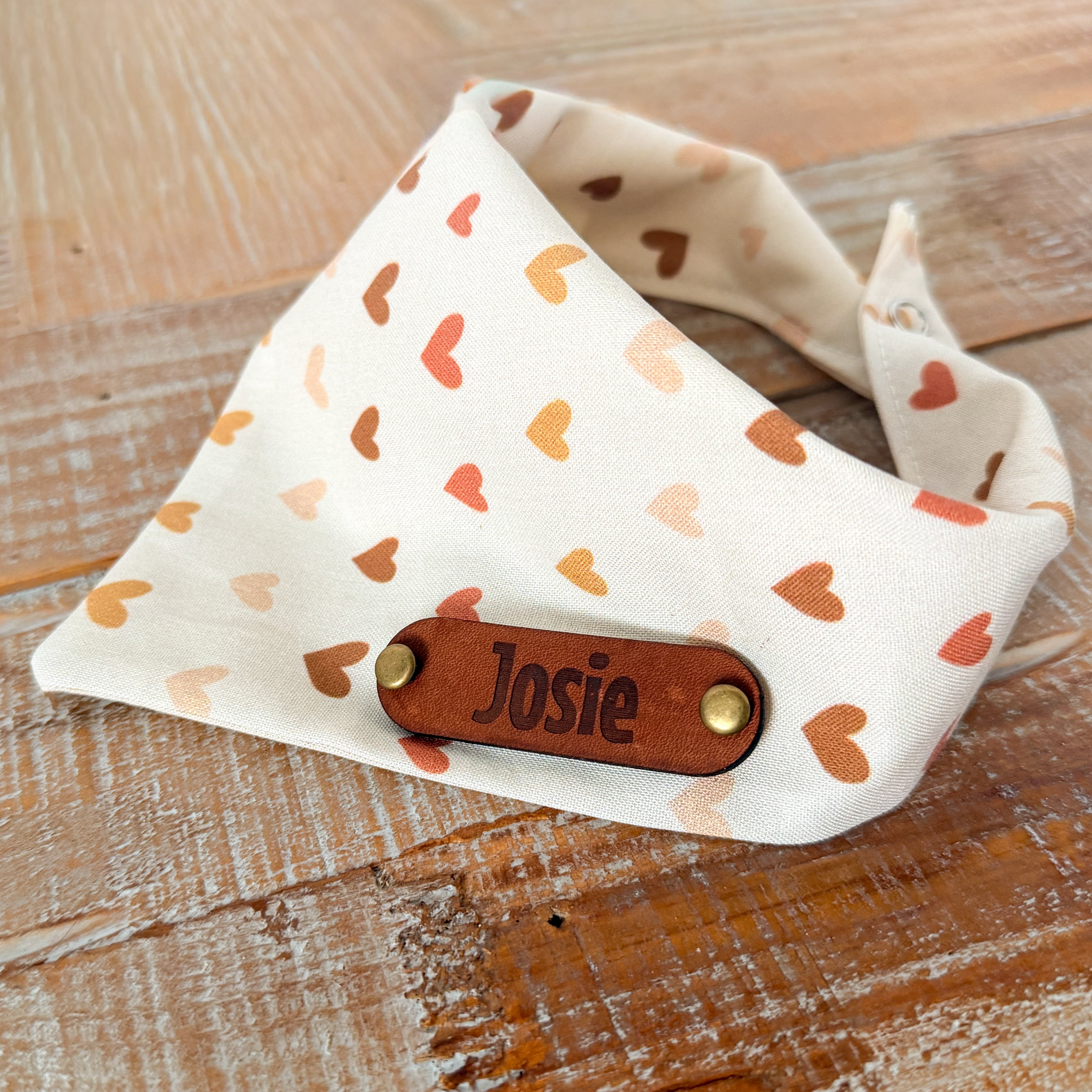Dog bandana with heart pattern and 'Josie' label on a wooden surface