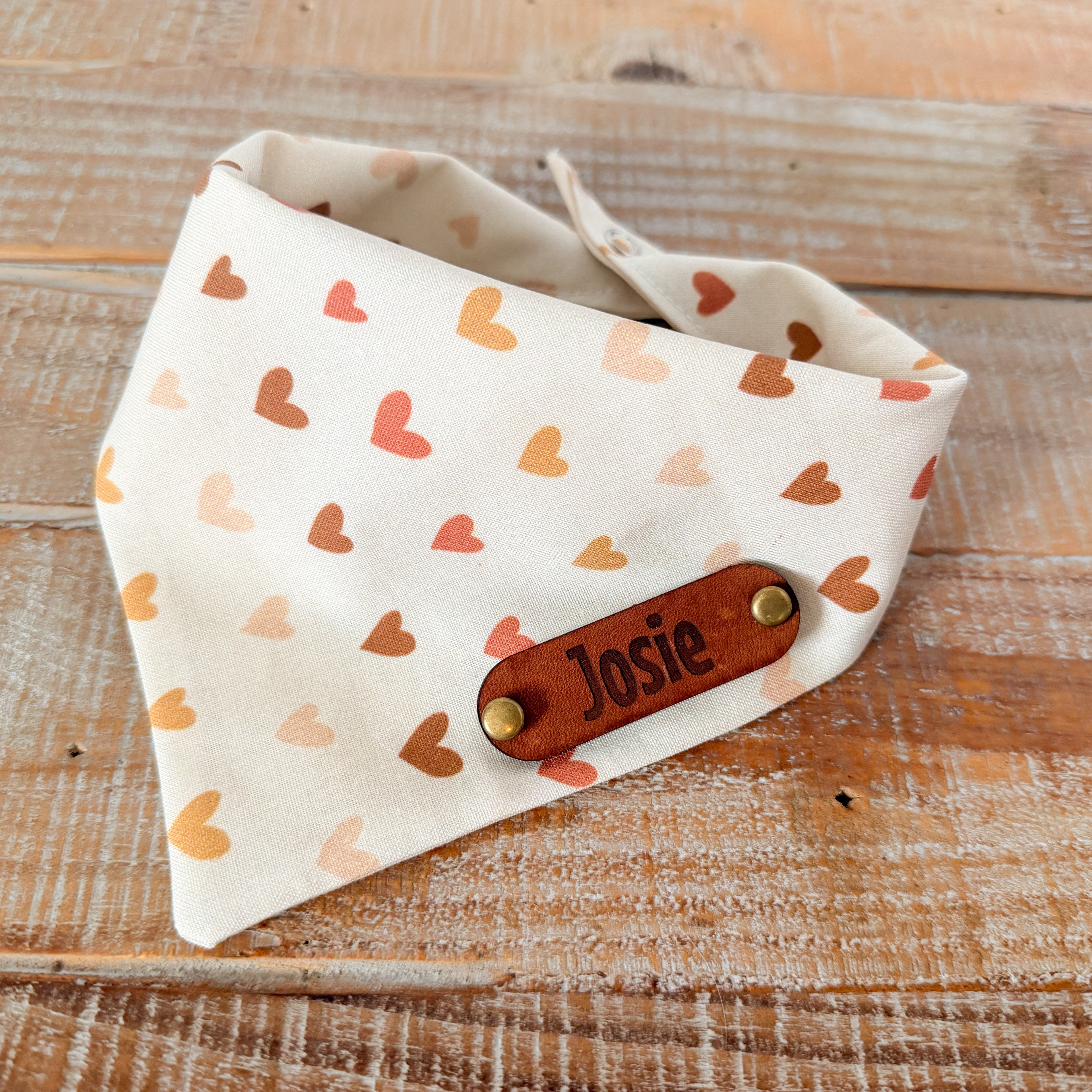 Dog bandana with heart pattern and 'Josie' tag on wooden surface
