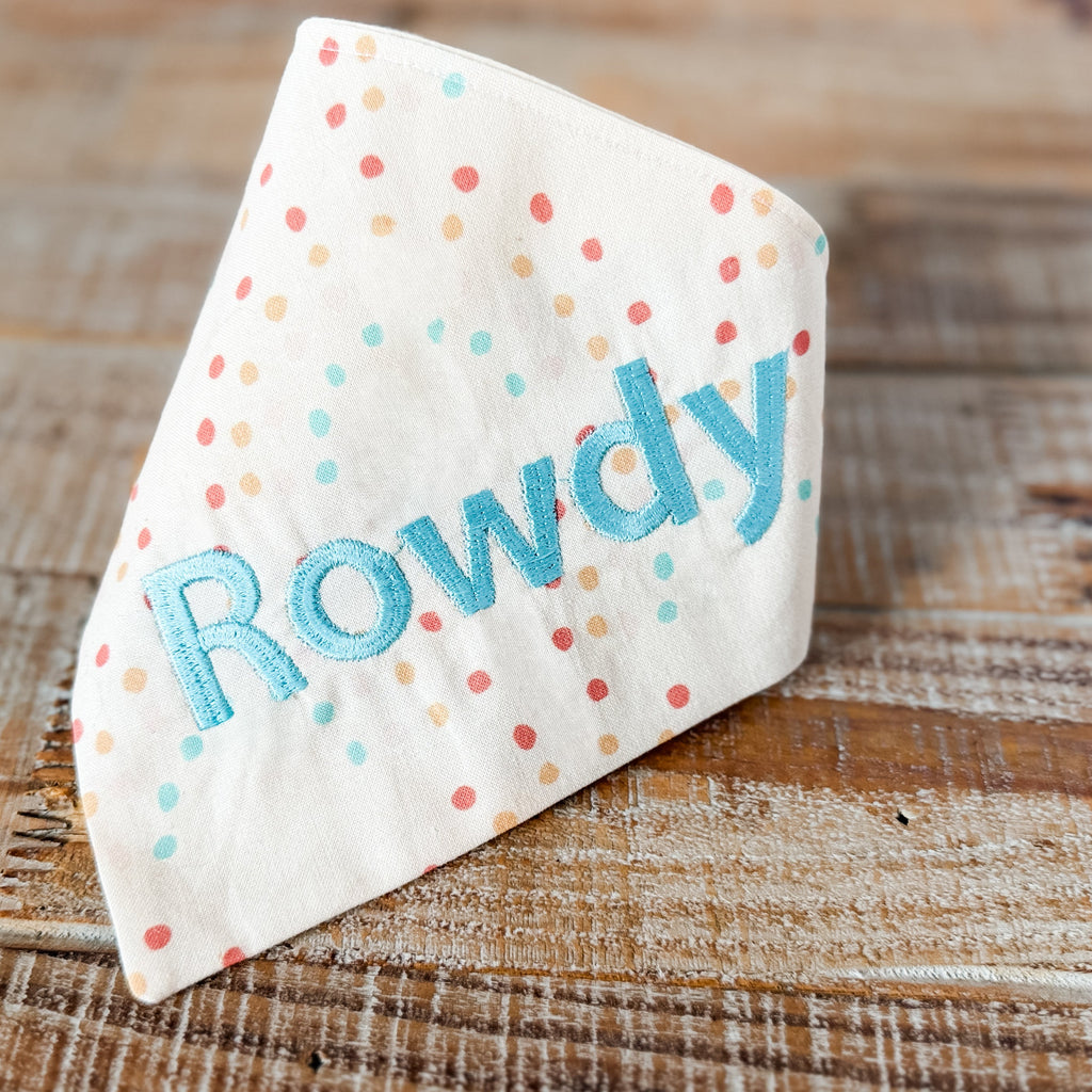 Dog bandana with 'Rowdy' embroidered on a wooden surface