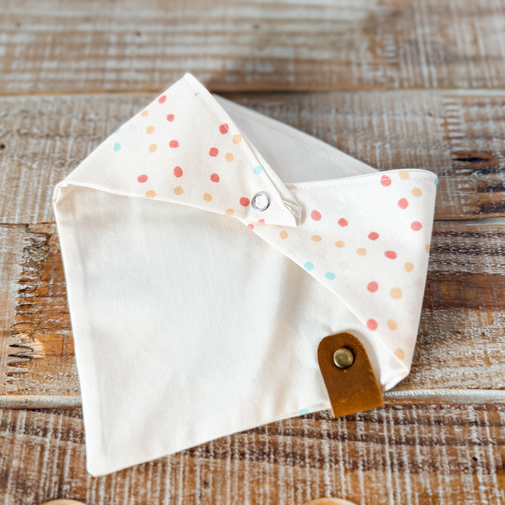 Small white pouch with colorful polka dots and a brown leather strap on a wooden surface