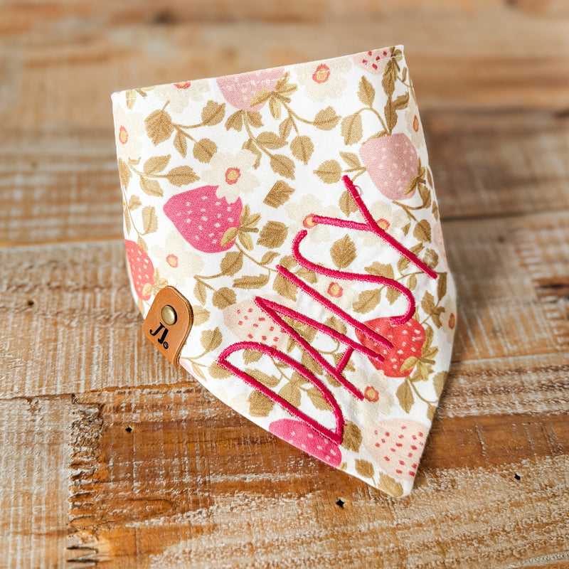 Floral patterned bandana with 'Milly' printed on it, placed on a wooden surface.