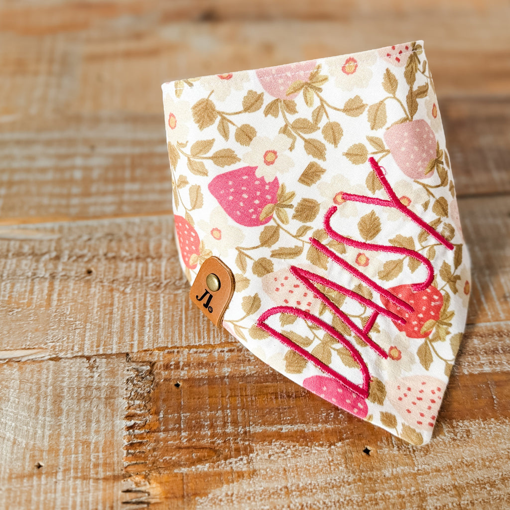 Floral patterned bandana with 'Milly' printed on it, placed on a wooden surface.
