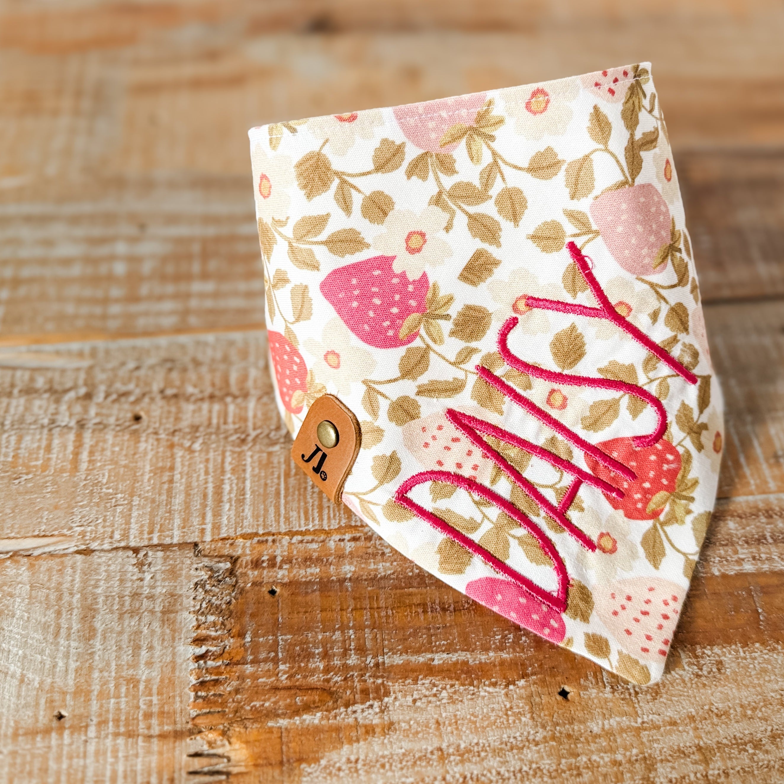 Floral patterned bandana with 'Milly' printed on it, placed on a wooden surface.