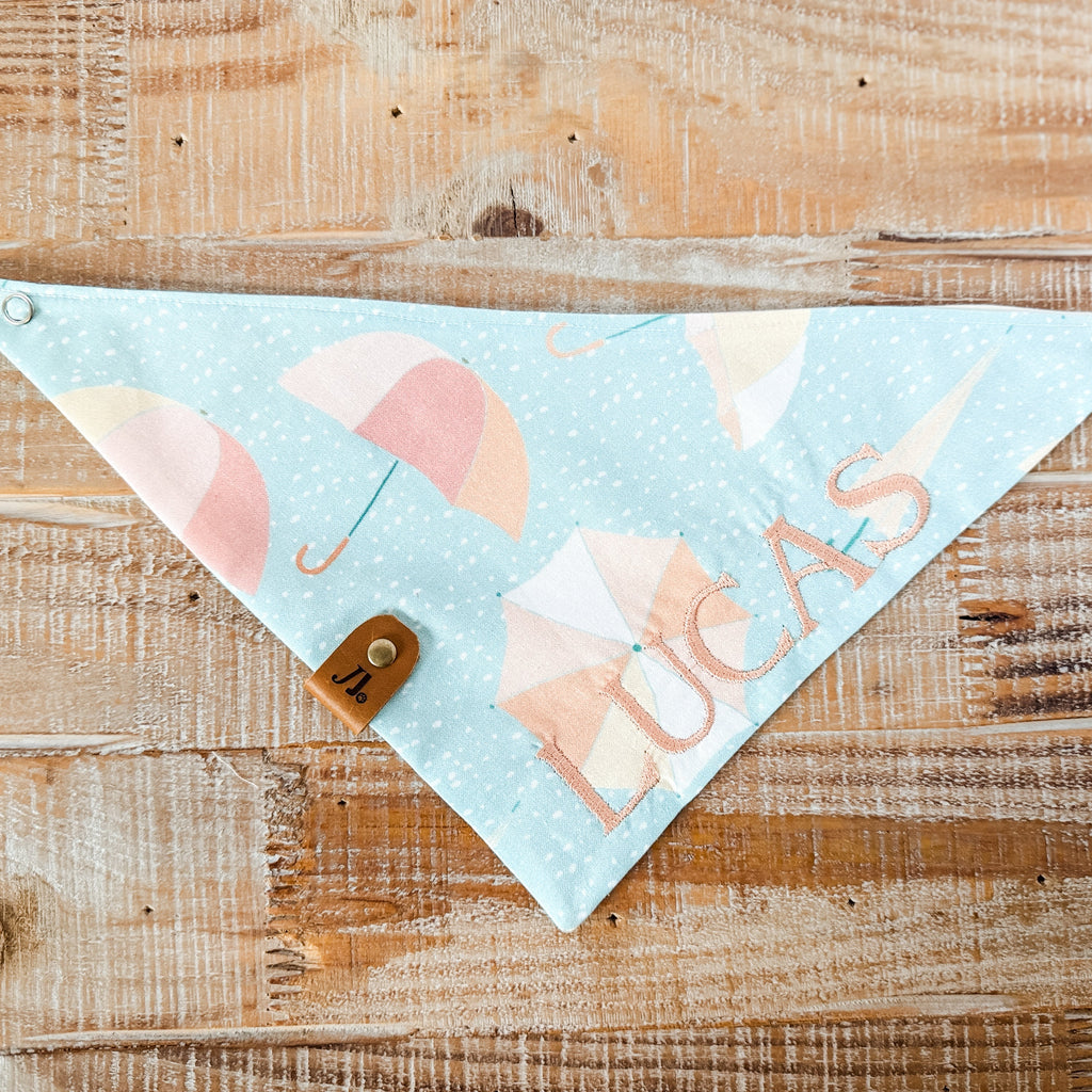 Baby bib with umbrella pattern and 'Lucas' text on a wooden surface