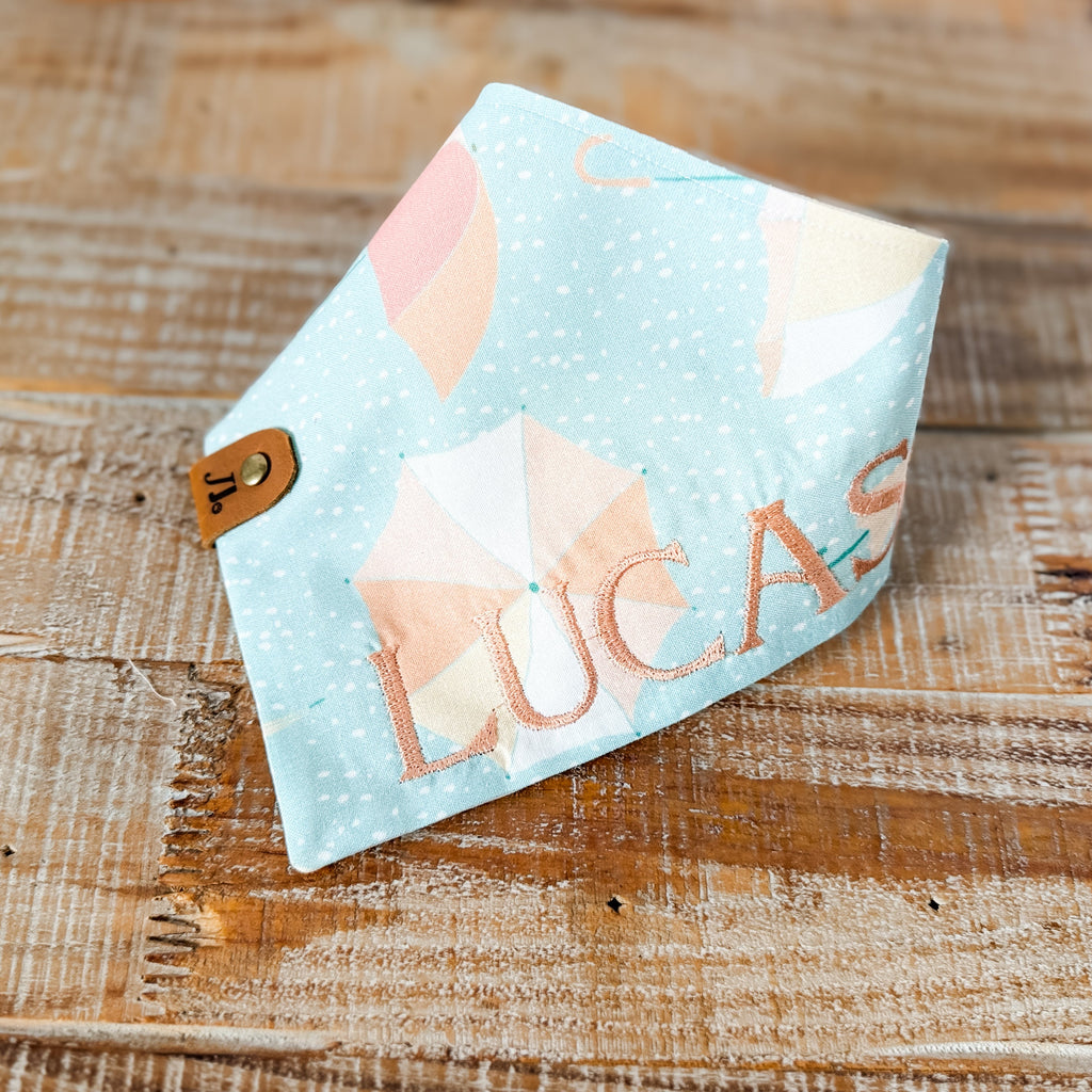 Baby bib with 'Lucas' printed on it, featuring clouds and stars design, on a wooden surface.