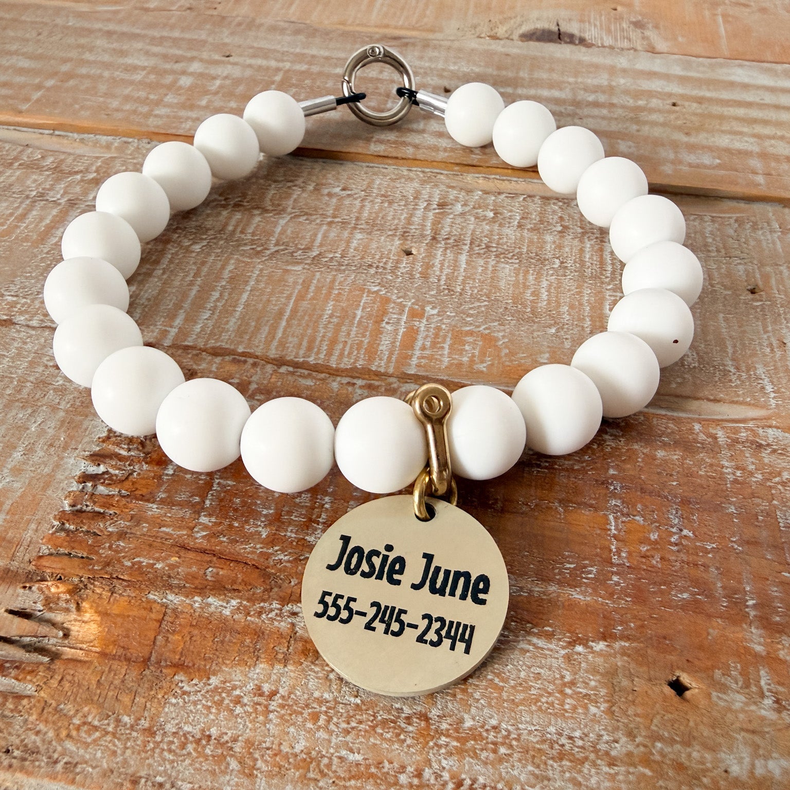 White beaded bracelet with a gold tag on a wooden surface